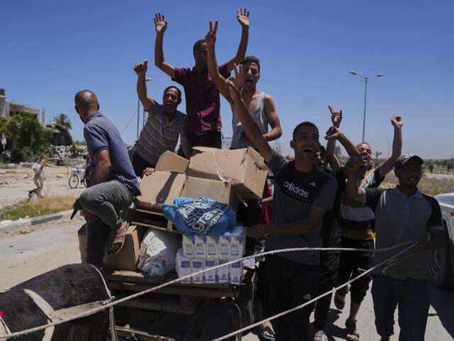 Palestinians wave to the camera as they carry boxes and bags containing food and humanitar